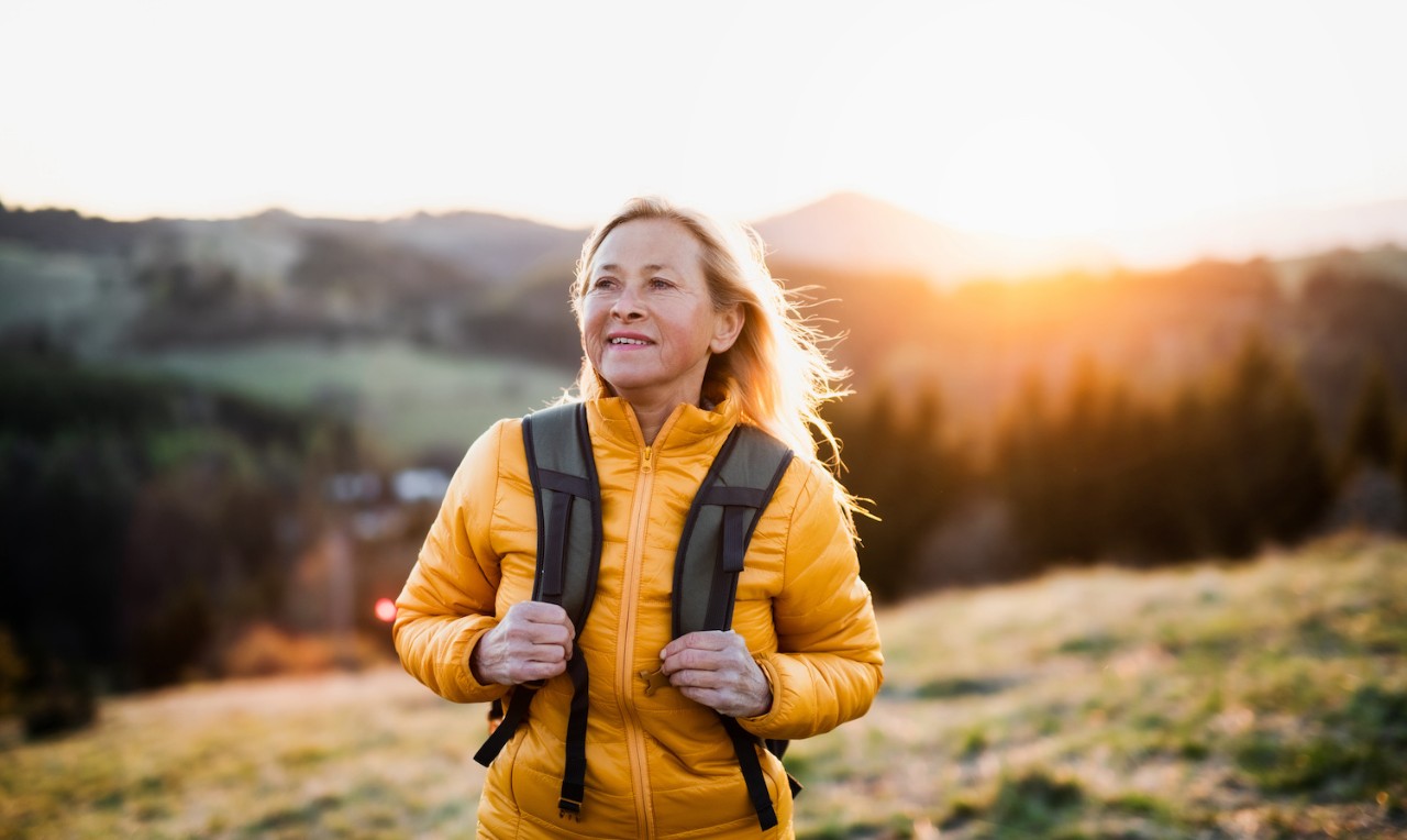 Attractive senior woman walking outdoors in nature at sunset, hiking.