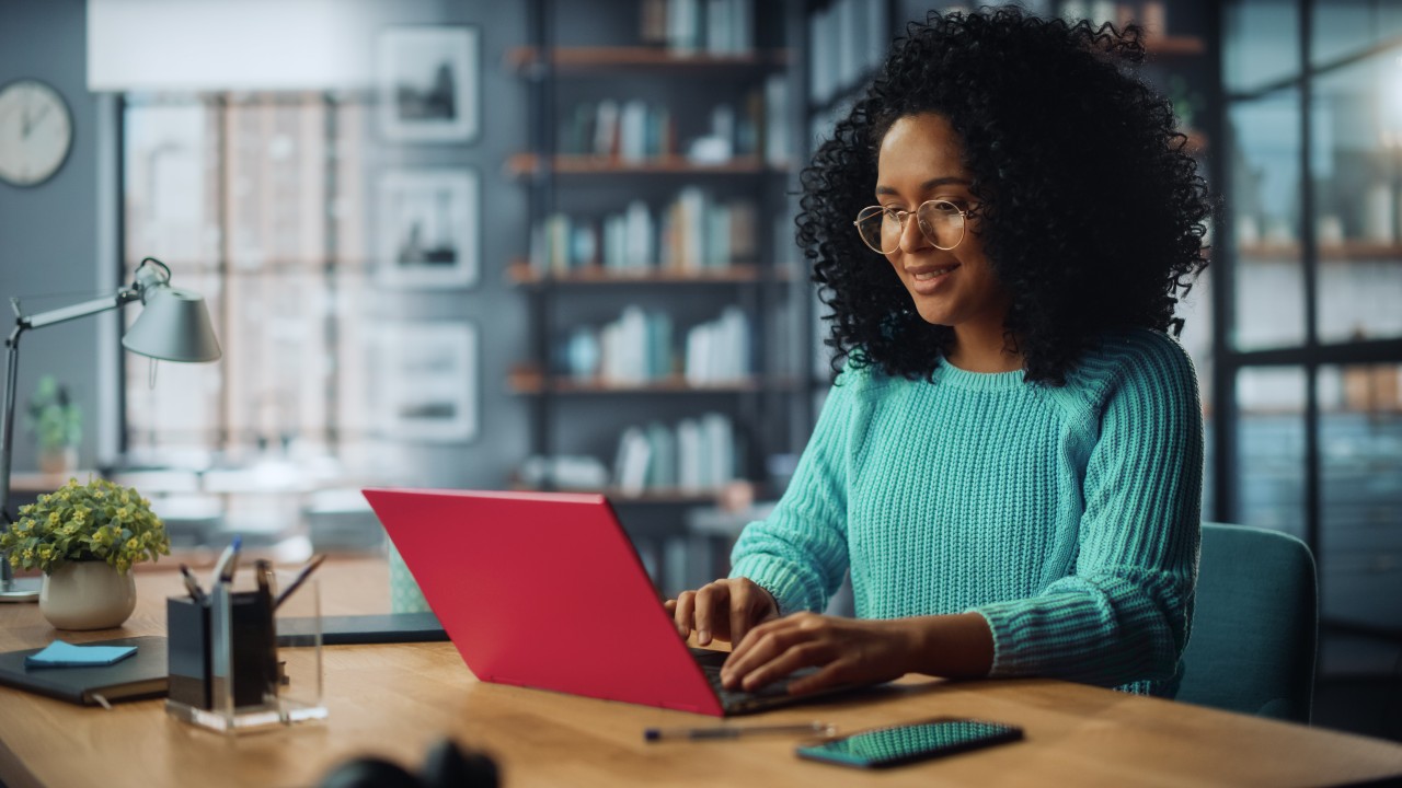women sitting behind a red laptop, typing on keyboard.